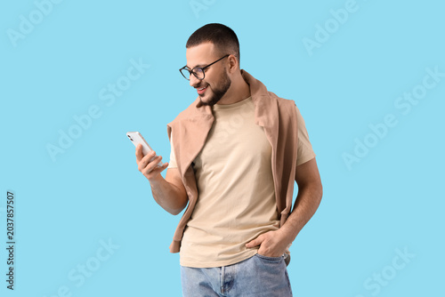 Handsome young man with mobile phone on blue background