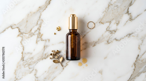 Essential oil bottle with herbs on marble.
