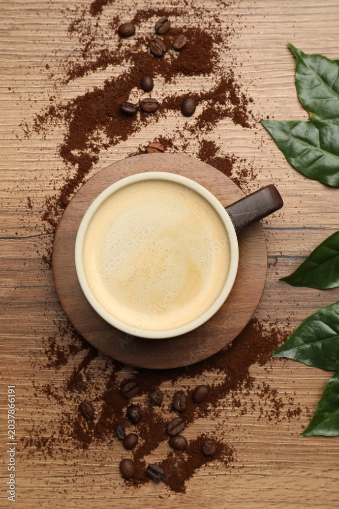 Obraz premium Cup of aromatic coffee, leaves and ground beans on wooden table, flat lay