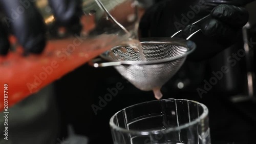 Barman colando líquido con colador metálico sobre fondo negro. Barman profesional filtrando un cóctel con un colador metálico. Cóctel artesanal, técnica de bar precisa, servicio de primera.