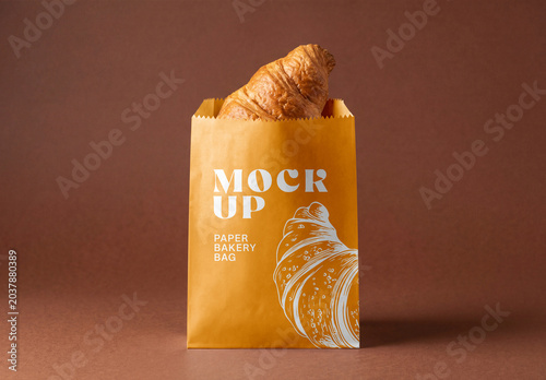 Brown kraft paper bakery bag mockup with fresh croissant inside isolated on a brown studio background