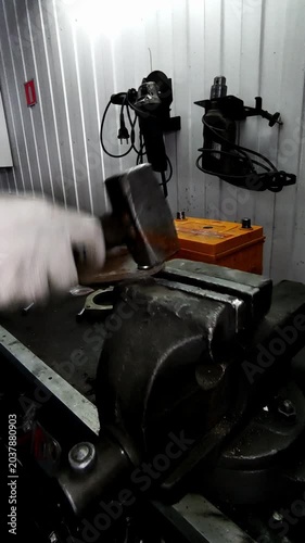  A gloved hand strikes a car part with a hammer
