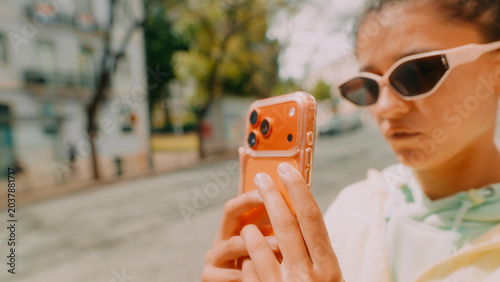 Young woman creator shooting street selfie with orange smartphone