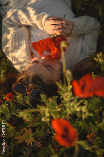 Portrait of little girl lying in blooming poppy field holding bouquet of red poppies and smelling flowers, warm childhood summer atmosphere and nature beauty concept