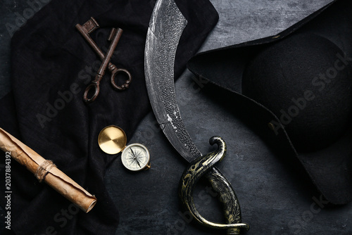 Fotografie Pirate hat, cutlass sword, old keys, compass and treasure map on dark background
