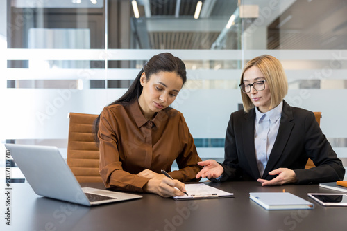 фотографія Two businesswomen collaborating on a project, reviewing important paperwork, wit