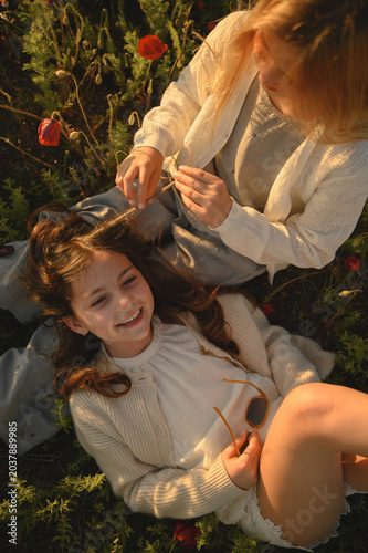 Two little girls laughing and hugging in blooming poppy field, playful childhood friendship moment filled with joy, warmth and carefree summer atmosphere