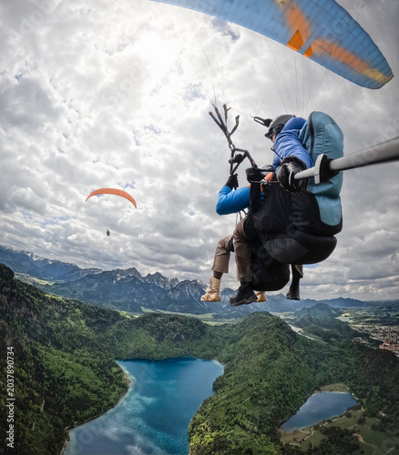 Fotografie Tandem paragliders flying above Alpsee lake and Schwangau ideal for outdoor adve