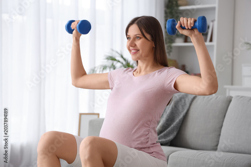 Sporty pregnant woman with dumbbells training at home