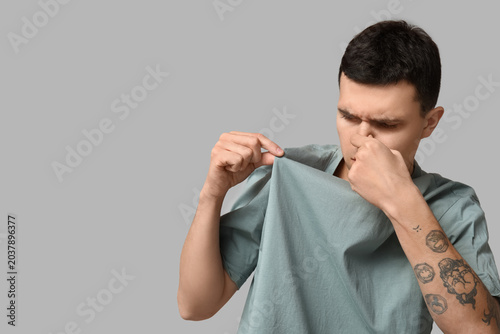 Quadro su tela Handsome young man feeling bad smell from dirty clothes on grey background