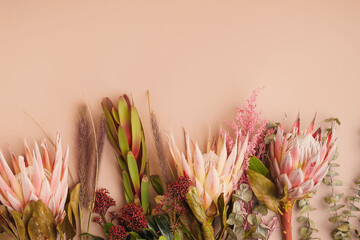 Tropical floral border with protea flowers, pampas grass and eucalyptus on beige background, pastel botanical arrangement with copy space