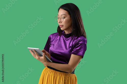 Beautiful stylish Asian woman with tablet on green background