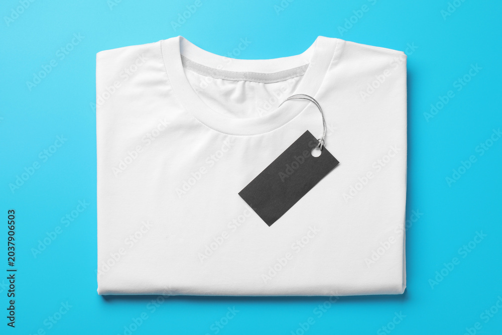 Naklejka premium Blank folded t-shirt with tag on light blue background, top view. Mockup for design