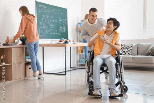 Photos Teenage boy with his classmate in wheelchair using mobile phone at school