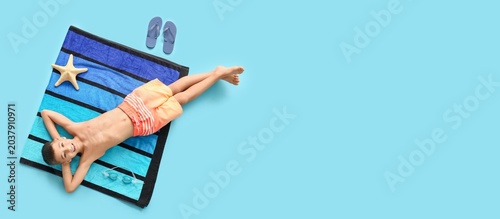 Cute little boy lying on beach towel against blue background with space for t...