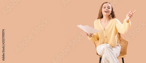 Φωτογραφία Beautiful actress with movie script sitting on chair against beige background wi