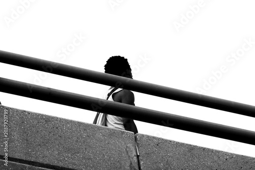 An artistic black and white image of an African American man walking across a bridge. 