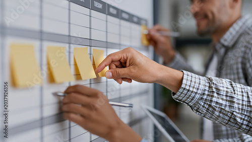 Office staff planning schedule with sticky notes on wall calendar