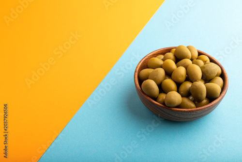 Fresh green olives in wooden bowl on blue and orange pastel paper. side view