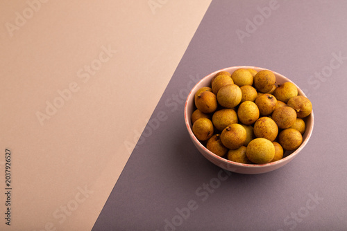 Ripe Longan in ceramic bowl on brown and gray pastel paper, side view, copy space