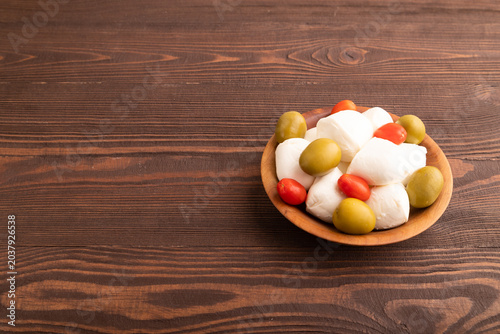 White Mozzarella cheese, with tomatoes and olives on brown wooden, side view, copy space.