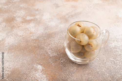 Ripe peeled Longan in glass on brown concrete, side view, copy space