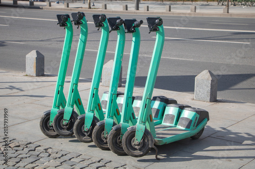 Row of shared electric scooters parked on an urban sidewalk near a city street in Bucharest, Romania, representing modern eco-friendly transportation.