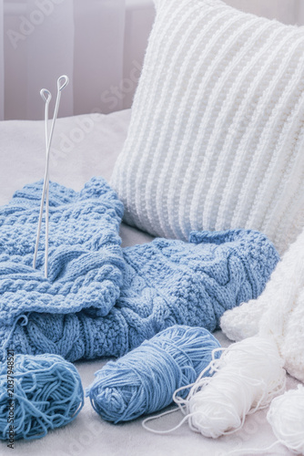 White knitted pillows with blue knitted textile, yarn balls and knitting needles on light background, cozy handmade knitting concept with copy space
