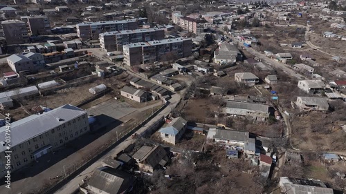A stunning aerial drone shot flying over a scenic mountain village with houses and apartments nestled in a snowy valley under a clear blue sky in beautiful Armenia.

