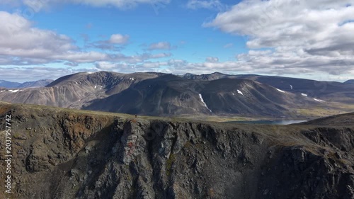 Aerial view of rocky ridge and bay in Russia, Chukotka, Provideniya bay. Side follow reveals cliff edge and distant peaks under daylight clouds. Wide shot frames vast arctic waterline to the horizon