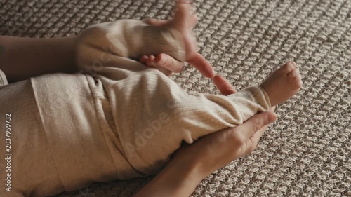Close up of mother hands gently touching and massaging moving legs and feet of newborn baby wearing knit pants on a textured blanket at home