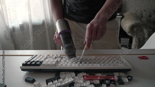 Hands cleaning keyboard, close up of hands removing white keycaps, scattered caps and tools on table, daylight through curtain, focused hobbyist performing precise