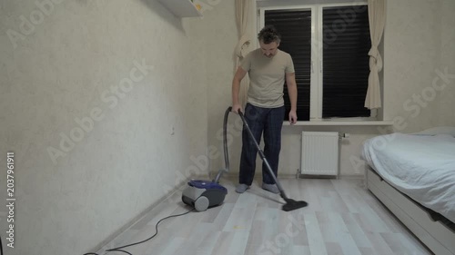 Man tidies up space. Young individual methodically cleaning minimalist bedroom during evening. Person in casual attire systematically vacuuming simple and quiet living space at dusk
