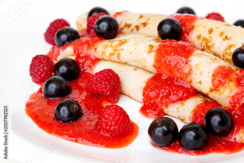 Close-up of golden thin pancakes covered with sweet raspberry syrup and fresh blackcurrants with raspberries.