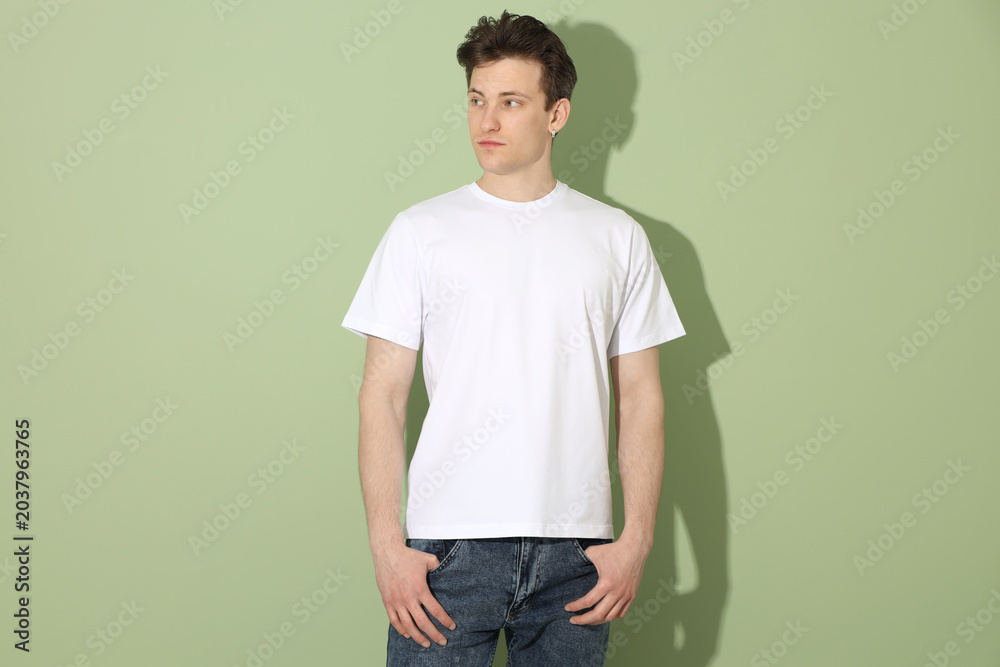 Fototapeta premium Handsome young man wearing blank white t-shirt on light green background. Mockup for design