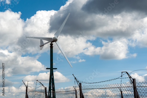 A small-scale horizontal-axis wind turbine (HAWT) set against a dramatic, cloudy sky