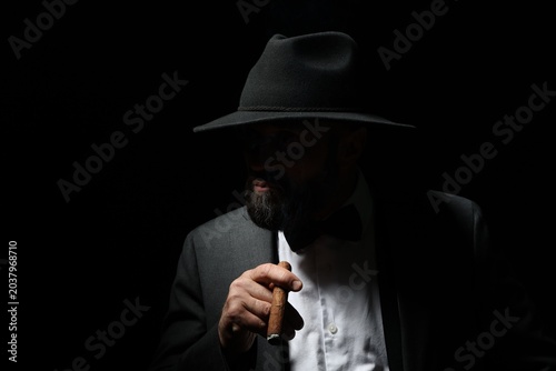 Tableau sur toile Mafia. Man in hat with cigar on dark background. Space for text