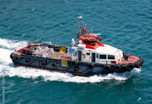 Small cargo workboat transporting freight across coastal waters with visible wake and marine equipment

Keywords: