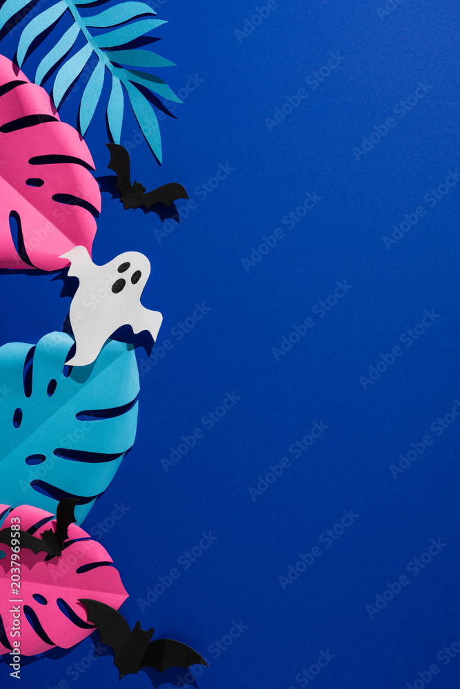 Obraz premium Tropical Halloween vertical paper ghost and bats among colorful monstera leaf on blue background