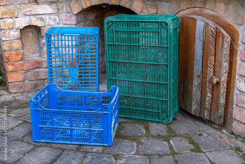 two green and one blue plastic crates in front of a brick wall