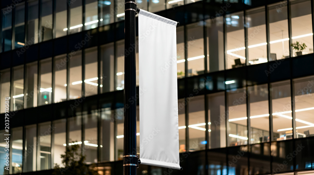 Obraz premium Blank white banner mockup hanging on a pole in front of a modern office building at night