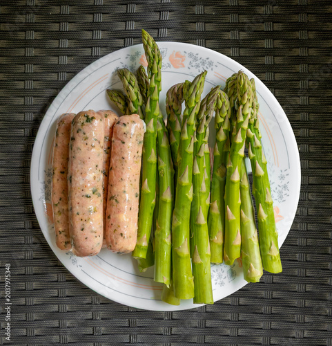 Herbed sausages and asparagus on a plate ready for grilling.