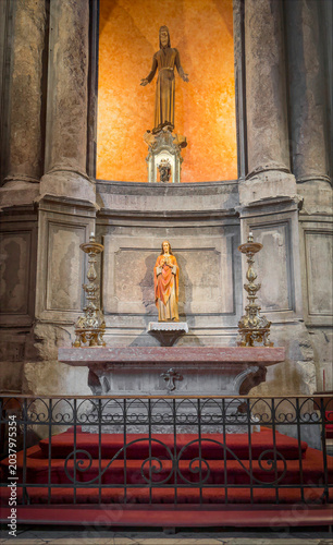 A detailed view of a church altar featuring two religious statues. The warm lighting enhances the ancient stone architecture and intricate candle holders.