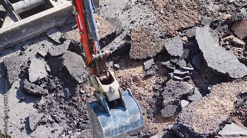 Orange excavator digging and scooping broken concrete debris at demolition site