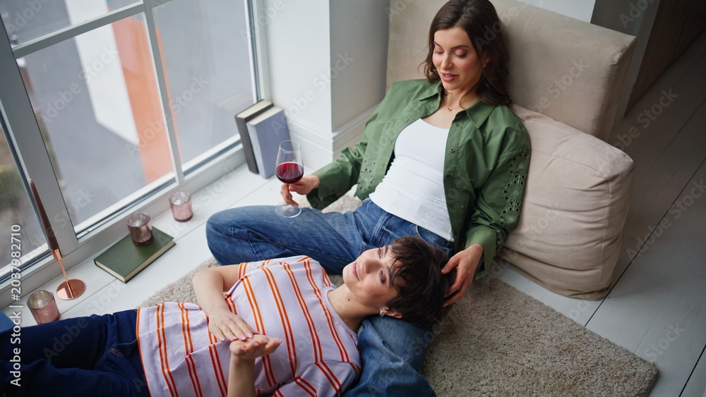 Obraz premium LGBTQ partners relaxing home talking enjoying calm weekend. Smiling brunette 