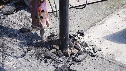 Pneumatic drill breaking concrete pavement at road repair site with dust