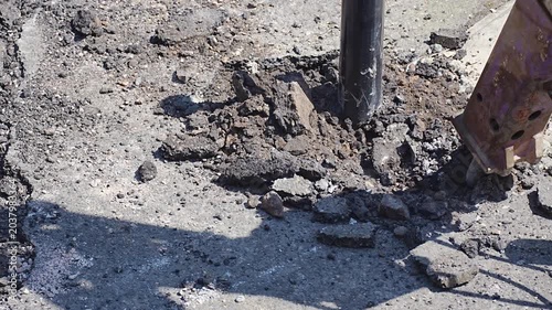 Hydraulic breaker drill pounding cracked concrete road surface at construction site