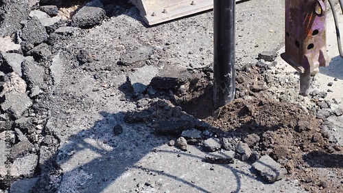Hydraulic breaker drilling into cracked concrete road surface at outdoor site