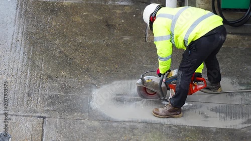 Construction worker cutting concrete pavement with circular saw at road site