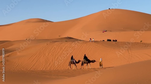 Camel caravan crossing Sahara dunes alongside modern desert adventure tourism